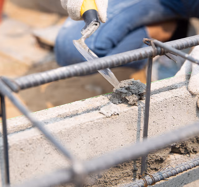 Maçon appliquant le mortier sur une assise de blocs béton, ferraillage et cordeau de niveau vert, sur un chantier à Aulnat